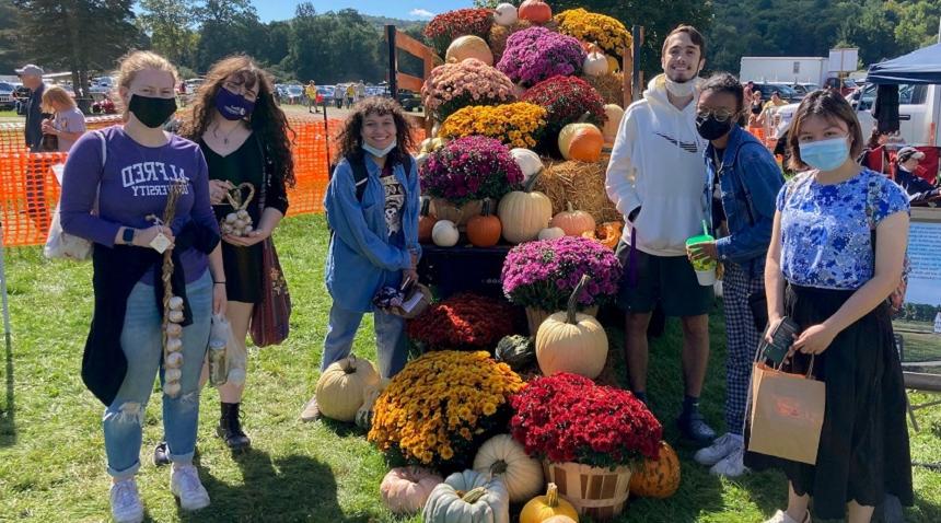 students at a fall festival with mums, pumpkins 和 garlic in their h和s